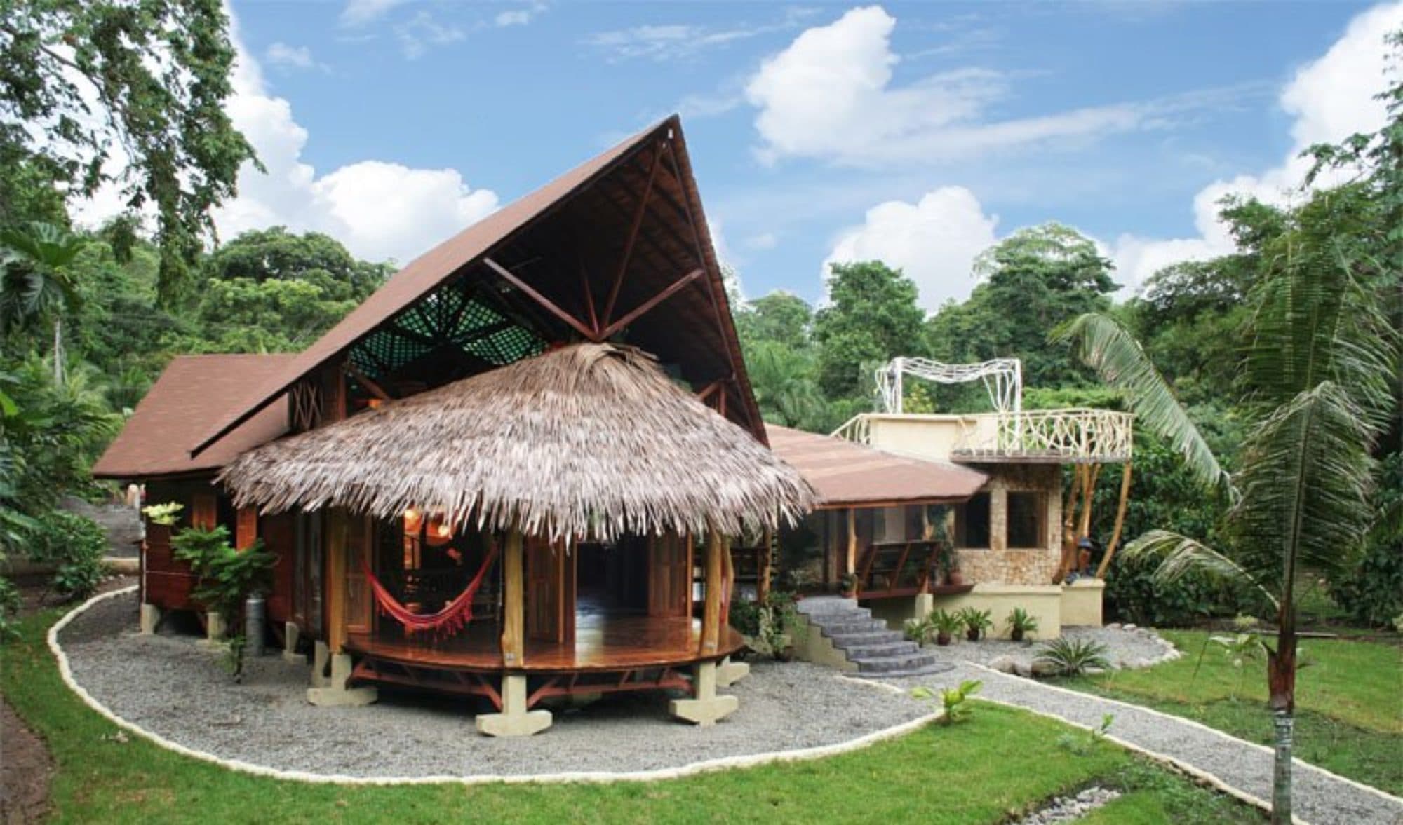 The Beach Suite's back façade — soaring A-frame roof, thatched rancho, mosaic outbuilding, framed by jungle and sky